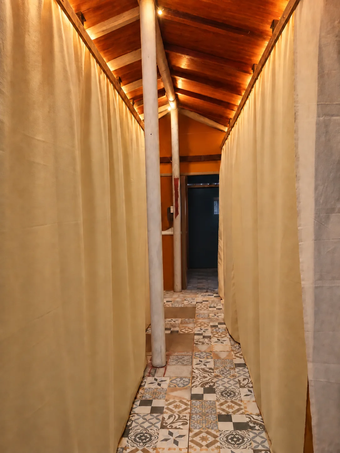 Pasillo interior del Hostel Kona Noho con cortinas a ambos lados y piso de baldosas decorativas